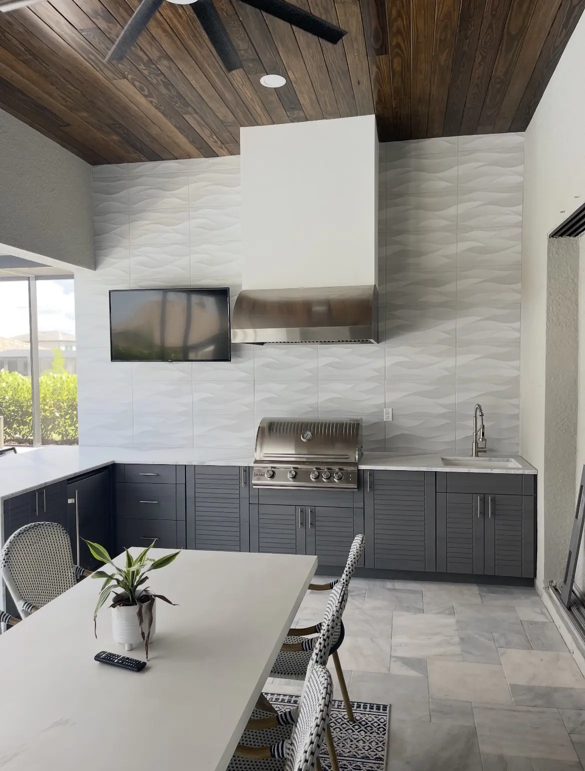 Completed outdoor kitchen with dark gray WeatherStrong cabinetry, grill, sink and tiled feature wall
