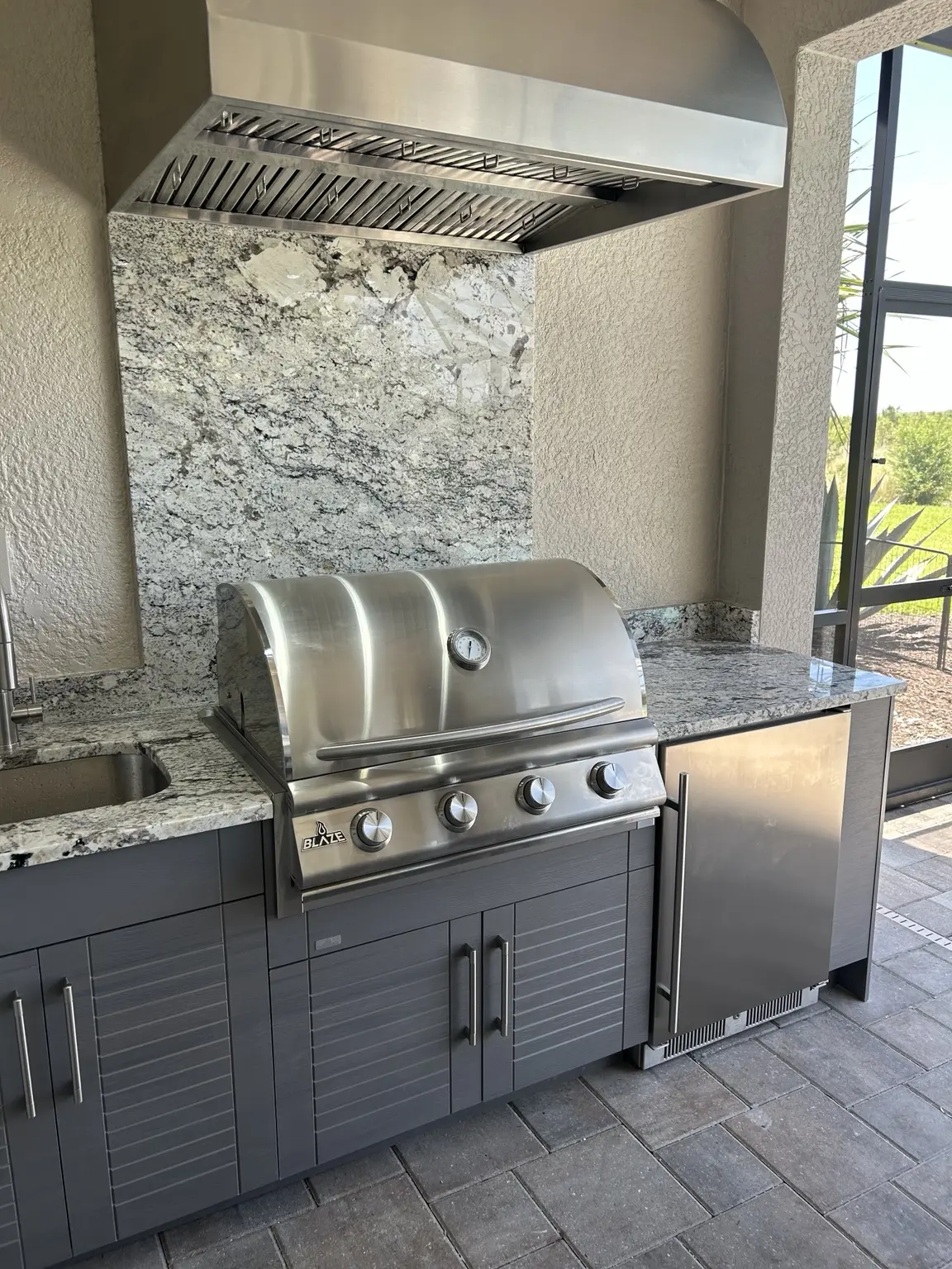 Outdoor kitchen with gray WeatherStrong cabinets, granite countertop, grill and ventilation hood